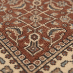 Close-up of a traditional patterned rug with a warm rust-brown field, cream borders, and muted blue-gray accents.