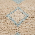 Close-up of a textured beige rug with a light blue geometric diamond pattern.