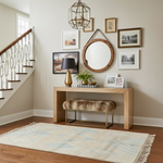 Entryway with wooden console table, mirror,  accent rug, and framed pictures on a beige wall.