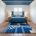 A blue and white geometric patterned area rug laid out on a terracotta tiled floor in a bright, modern bedroom with a blue bed and white walls.