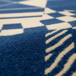 Close-up of a textured blue and cream geometric patterned rug, showing the detailed pile and color contrast.