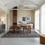 A modern dining room with a wooden dining table and four matching chairs on a dark gray patterned rug. The room features a high white-beamed ceiling, beige walls, a dark red vertical slatted accent wall, and large windows with white curtains.