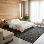 A modern bedroom interior featuring a low wooden platform bed dressed in white linens and a cream throw, set on a dark charcoal rug with tan geometric accents. The room has a light wood plank accent wall, a tall narrow window, sheer white curtains, and a white sculptural chair.