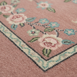 Close-up of a dusty pink area rug with a floral pattern and a decorative border in cream, light blue, and green.