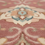 Close-up of a plush area rug with a traditional floral and scroll pattern in dusty pink, cream, light blue, and soft peach tones.