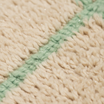 Close-up of a chunky knit textile with a warm cream-beige body and a diagonal mint green stripe, showing the soft woven texture and small reflective glitter flecks.