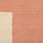 A close-up of a textured woven rug showing a terracotta pink field with a cream-colored corner block.
