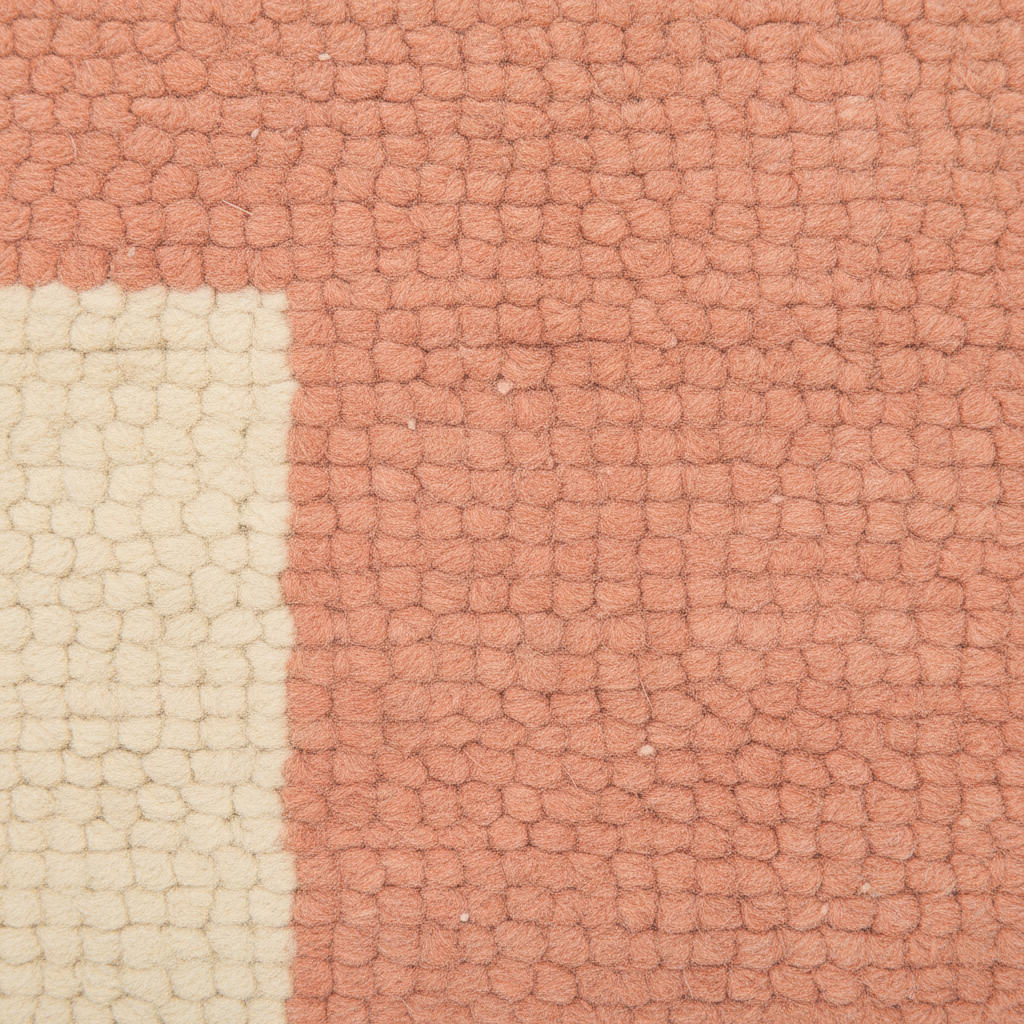 A close-up of a textured woven rug showing a terracotta pink field with a cream-colored corner block.