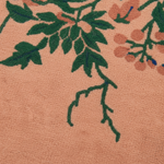 Close-up of a textured peach-pink fabric with a raised floral pattern in dark green leaves and muted coral-pink blossoms.