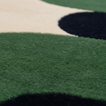 Close-up of a plush area rug with a modern abstract pattern of green, cream, and black organic shapes.