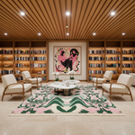 A modern living room with a large pink, green, and cream patterned area rug, surrounded by four cream armchairs with wooden frames. The room features a slatted wood ceiling with recessed lights, built-in wooden bookshelves filled with books, and a central framed art print.