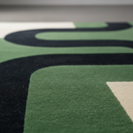 Close-up of a modern area rug with a bold geometric pattern in forest green, black, and cream, showing the soft texture of the pile.