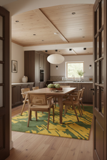 A modern dining room scene viewed through an open doorway, featuring a wooden dining table and chairs on a yellow and green patterned rug. The room has light wood ceiling panels, a white pendant light, and a contemporary kitchen in the background.