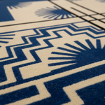 Close-up of a textured rug with a bold geometric pattern in deep blue and cream, featuring sunburst and chevron motifs.