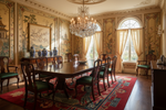 Grand dining room with ornate walls, a chandelier, chinoiserie red rug, and a large table with chairs.
