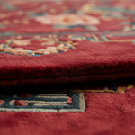 Close-up of a folded red patterned rug showing the plush pile texture and part of a traditional floral and geometric design.