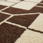 Close-up of a textured area rug with a geometric diamond pattern in dark brown and cream.