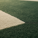 Close-up of a textured area rug with a dark green field and a contrasting cream-colored geometric section.