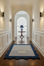 Hallway with a decorative rug featuring text, wooden table, and lamp in the background.