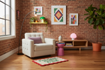 A styled living room corner with a white tufted armchair, pink side table, brick wall, wood floor, framed art, floor lamp, and potted plant. A rug on the floor reads 'PRACTICE WHAT YOU BELIEVE.