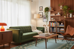 A cozy, mid-century modern living room featuring a green tufted sofa, a wooden coffee table, a brown leather chair, and a slatted wood wall with shelves and plants.
