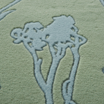 Close-up of a textured area rug featuring a stylized tree design in a muted sage green and pale blue-gray colorway.