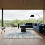 A modern living room with a large blue sectional sofa, matching blue accent chair, patterned blue and beige rug, black floor lamp, and a large wood ceiling and floor overlooking a forest view.