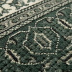 Close-up of a textured area rug with a traditional geometric pattern in dark forest green and cream.