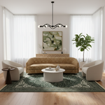 A styled living room featuring a central patterned beige sofa, two cream armchairs, a white ribbed coffee table, a green patterned area rug, and a large potted fiddle-leaf fig plant. The room is decorated with white sheer curtains, a black multi-arm chandelier, and a framed abstract painting on the wall.