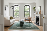 Modern living room with a green knotted traditional rug, white sofa, and wooden chair.