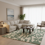 A modern living room featuring a large geometric area rug in sage green and cream, styled with a light beige sectional sofa, a dark wood coffee table, and a potted plant.