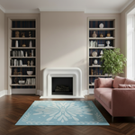 A styled living room scene featuring a light blue and white patterned area rug on a dark wood herringbone floor, positioned in front of a white fireplace. To the right is a dusty pink sofa, and the background consists of tall built-in shelves with navy blue backing and neutral decor.