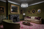 Luxurious living room with pink rug, green walls, a chandelier, and classical decor.