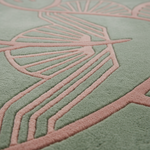Close-up of a textured rug with a muted sage green base and a raised dusty pink geometric leaf-like pattern.