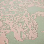 A close-up of a textured rug featuring a stylized animal pattern in pale pink raised relief on a soft mint green background.