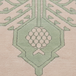 Close-up of a patterned rug with a pale pink field, sage green geometric border, and a central cluster of cream circular motifs.