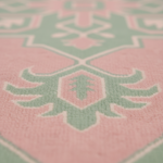 Close-up of a soft textile surface with a repeating geometric and floral-inspired pattern in pink, pale green, and off-white, shown in shallow depth of field.