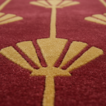 Close-up of a textured area rug featuring a deep burgundy red background with a raised gold geometric floral pattern.