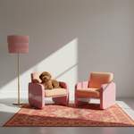 Two modern pink armchairs with peach cushions are arranged on a patterned rug in a minimalist room. A small brown dog sits in the left chair, and a pink floor lamp stands to the left.