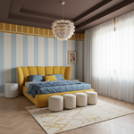 A modern bedroom interior featuring a bright yellow upholstered bed frame with blue patterned bedding, four matching cream ottomans, a striped accent wall, and a white flower-shaped pendant light.