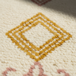 Close-up of a textured cream rug with a mustard yellow geometric diamond pattern and soft pink accents.