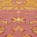 Close-up of a patterned area rug with a dusty pink field, yellow-gold floral motifs, and a yellow border.