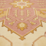 Close-up of a patterned rug with a dusty pink and cream base and mustard yellow geometric and floral motifs.