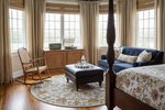 Luxurious bedroom with a four-poster bed, rocking chair, round floral beige rug, and wooden cabinet.
