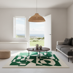 A modern living room with a large area rug featuring a bold green and cream geometric pattern. The rug is styled under a round wooden coffee table, with a gray sofa, a woven pendant light, and an open white door revealing a scenic view of the sea and grassy hills in the background.