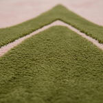 Close-up of a plush textured rug in olive green with a contrasting light pink border.