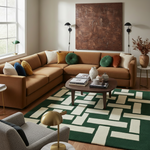 A styled living room featuring a large tan sectional sofa with multiple accent pillows, a green and cream geometric patterned area rug, a dark wood coffee table, and a large textured brown wall art piece.