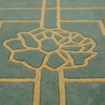 Close-up of a textured rug with a sage green background and a raised tan geometric floral pattern.