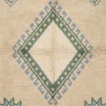 A close-up of a textured rug featuring a central diamond motif in cream, sage green, and light blue, with geometric patterns in the corners.