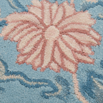Close-up of a textured area rug featuring a large pink and cream floral motif on a light blue background.